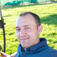 Man in a blue shirt sitting outdoors with green grass in the background