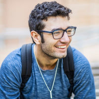 Man wearing glasses and a blue shirt with a backpack, smiling outdoors.