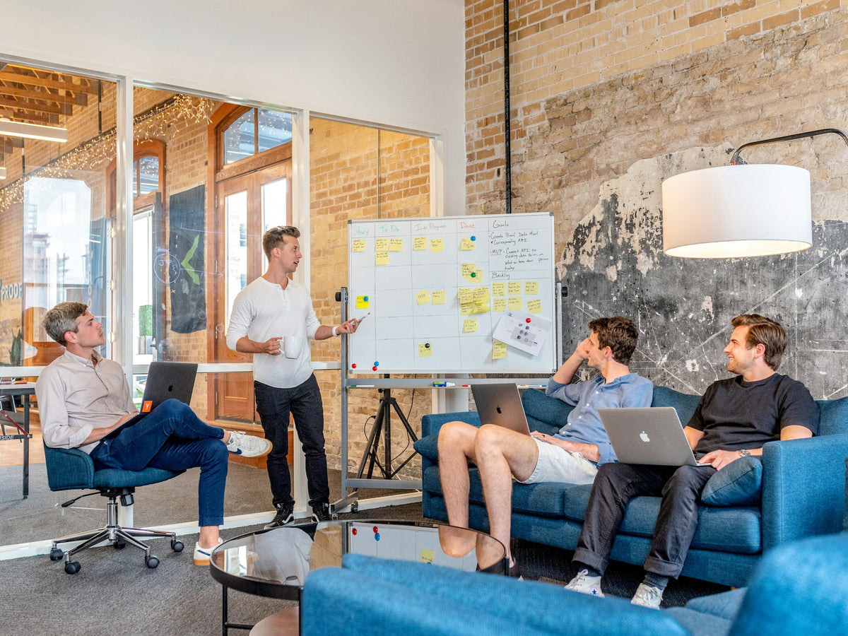 Group of people in a modern office setting with a whiteboard and laptops.