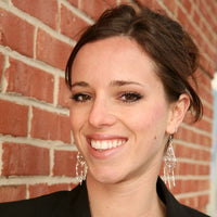 Woman with earrings smiling in front of a brick wall