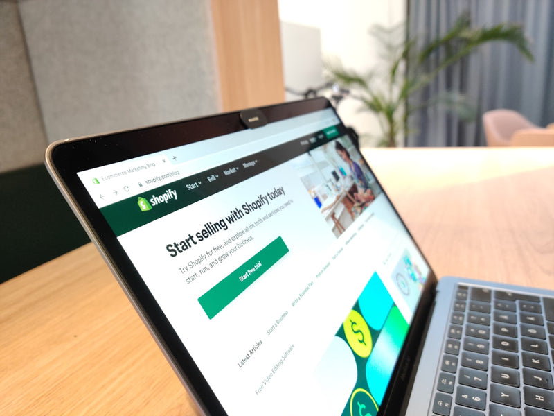 Laptop displaying the Shopify website on a wooden desk.