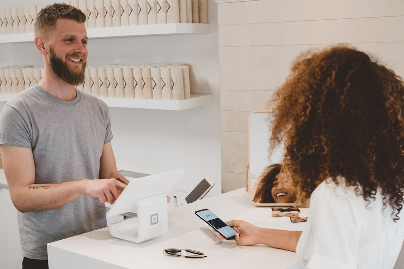 Man using a smartphone at a counter with a woman, possibly in a retail or service setting.