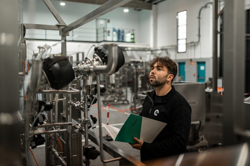 Man in a factory setting holding documents and looking at machinery