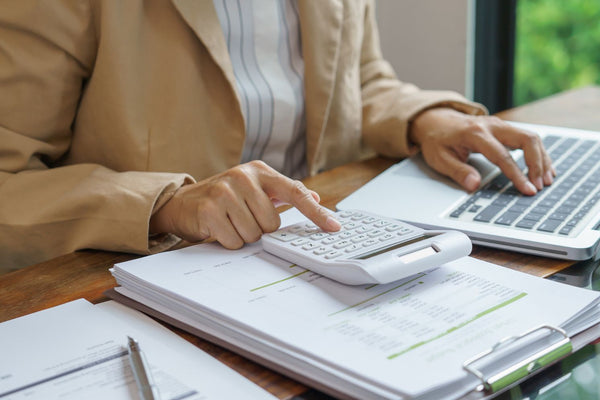 Person using a calculator and laptop on a desk with books and stationery.