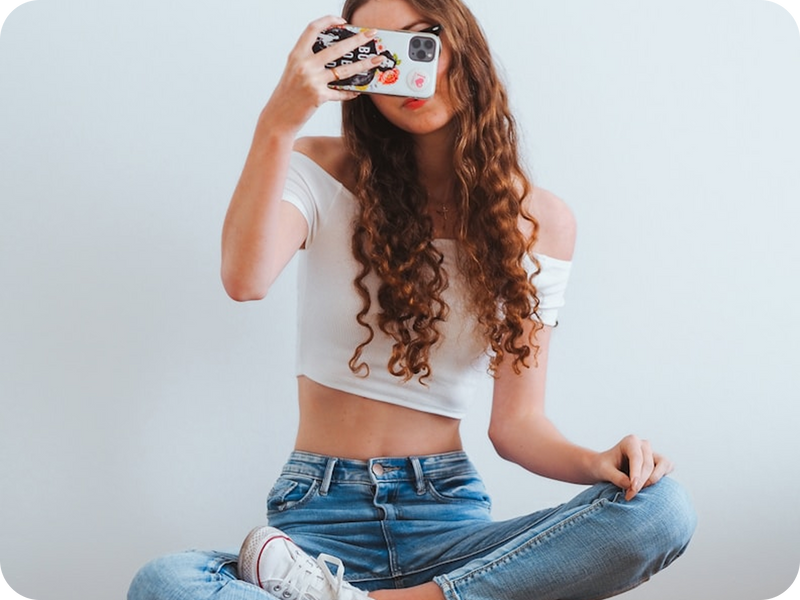 Person taking a mirror selfie wearing a white crop top and blue jeans.