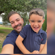 Man and young boy in matching navy blue polo shirts outdoors with greenery in the background