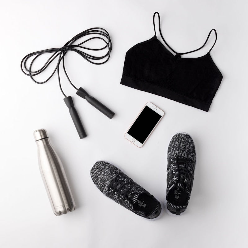 Flat lay of fitness items including a sports bra, jump rope, water bottle, and slippers on a white background