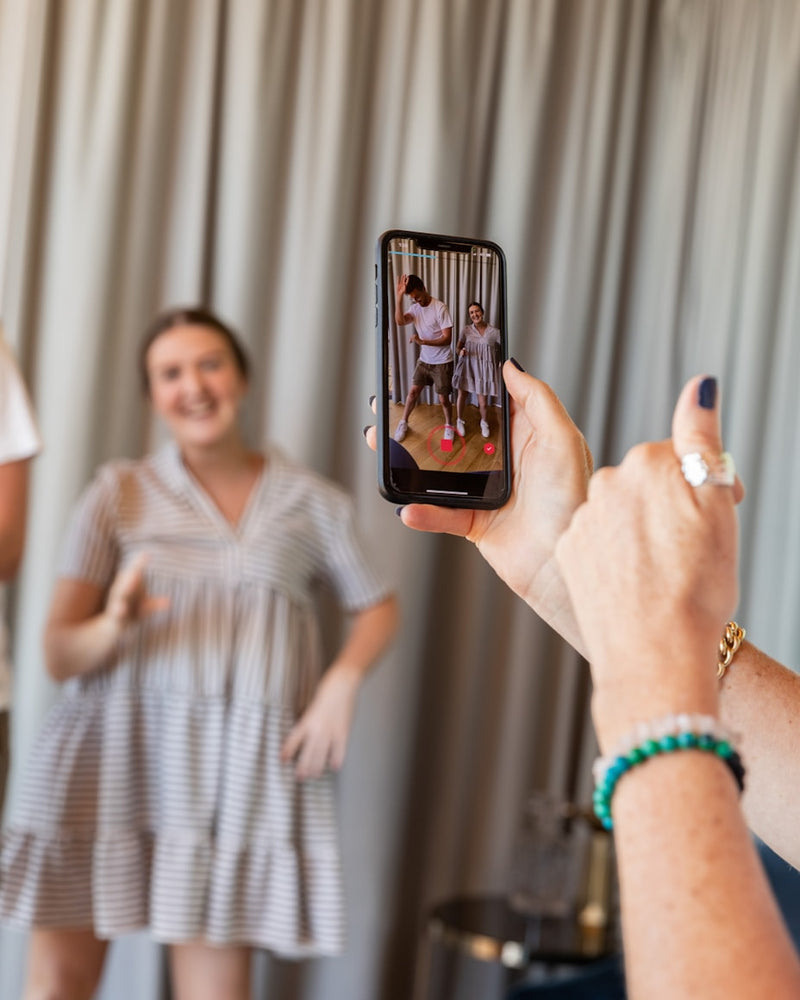 Person taking a photo of another person wearing a dress with a smartphone.