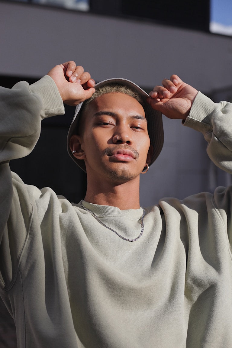 Person wearing a light gray hoodie and cap, standing against a dark background