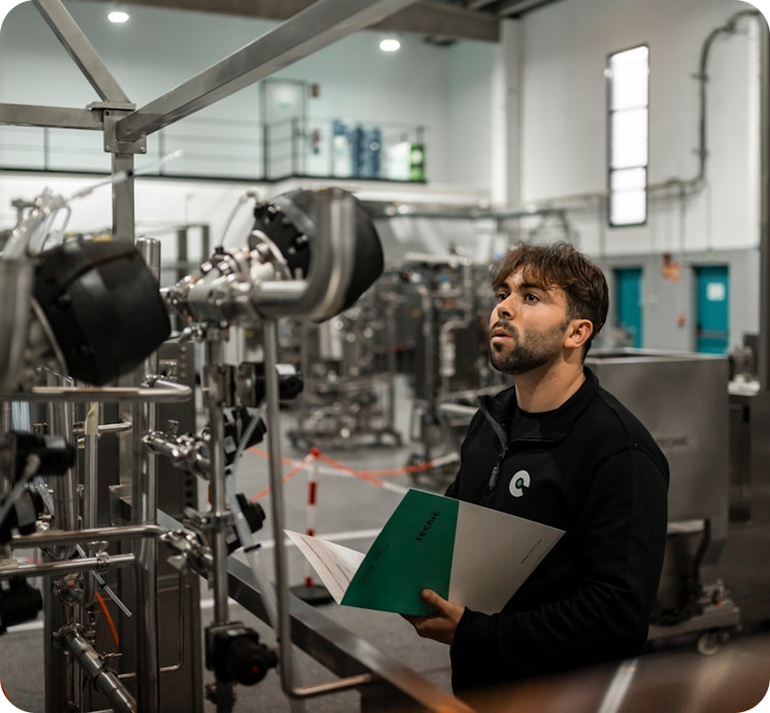 Man in a factory setting looking at machinery with a notebook